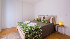 A bedroom with a bed, a wardrobe, a bedside table with a lamp, and a hanging light fixture. - Botanic Garden Duplex (Ponta Delgada)