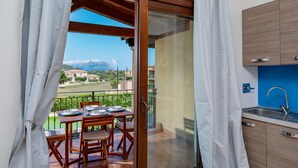 A balcony with a dining table and chairs, a sliding glass door, and a view of a mountain range.