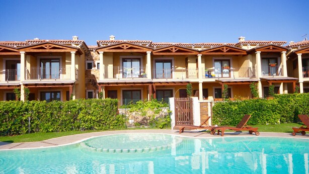 A hotel with multiple balconies, a swimming pool, and a well-maintained garden.