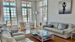 A spacious living room with a white sofa, a glass coffee table, and a view of the outdoors through large windows. - Les Pieds Dans L'eau, la Tête Dans les Étoiles (HYERES)