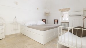 A white bedroom with a bed, bedside tables, a lamp, and an air conditioning unit. - Casa Carducci by Wonderful Italy (Ostuni)