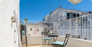 An outdoor balcony with a table and chairs, a white railing, and a clear blue sky.