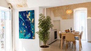 A modern kitchen with a dining area, a large abstract painting, and a potted plant.