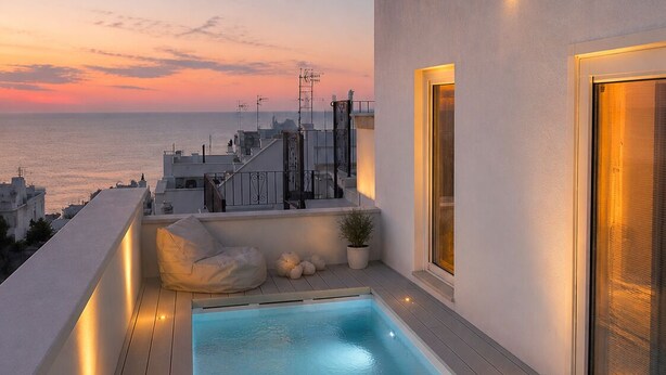 A rooftop pool with a view of the sea at sunset, surrounded by modern architecture.