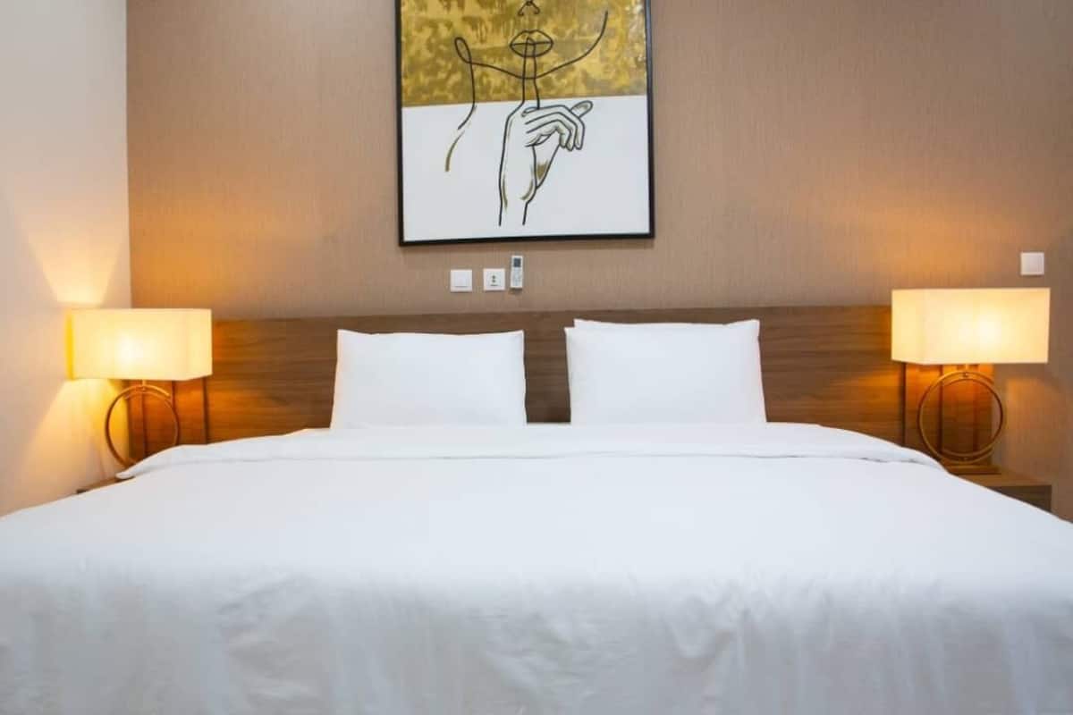 A hotel room with a large bed, two bedside lamps, and a framed artwork on the wall.