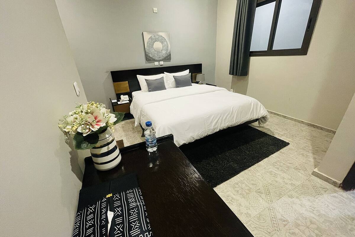 A hotel room with a bed, bedside table, water bottle, and a vase of flowers.
