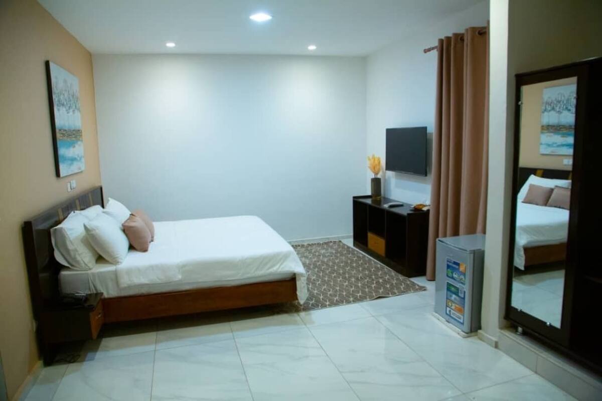 A hotel room with a bed, a nightstand, a TV, a mirror, and a small cabinet.