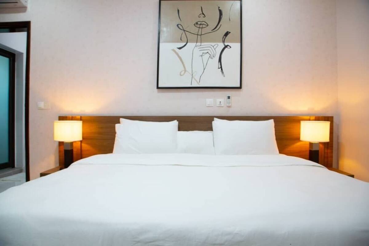 A hotel room with a large bed, two bedside lamps, and a framed abstract artwork on the wall.