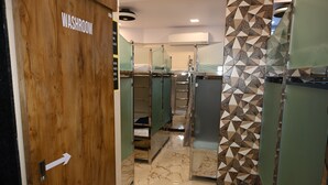 A hotel bathroom with a wooden door labeled "WASHROOM," glass-enclosed shower stalls, and a patterned tile floor. - Sagar Dormitory Andheri - Nearest to Andheri Railway Station West (Mumbai)