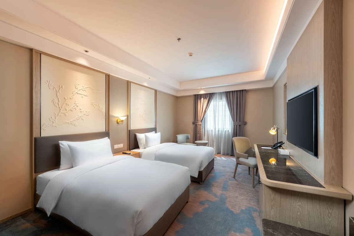 Ein Hotelzimmer mit zwei Betten, einem Schreibtisch, einem Fernseher und einem Sessel.