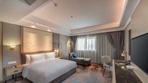Habitación de hotel con una cama grande, un escritorio con silla, una mesita y un televisor.