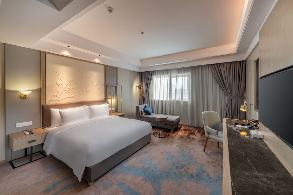 Ein Hotelzimmer mit einem großen Bett, einem Schreibtisch mit Stuhl, einem kleinen Tisch und einem Fernseher.