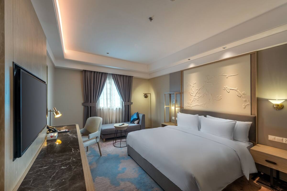 Ein Hotelzimmer mit einem großen Bett, einem Schreibtisch, einem Flachbildfernseher, einem Sessel, einem kleinen Tisch und einer Couch.