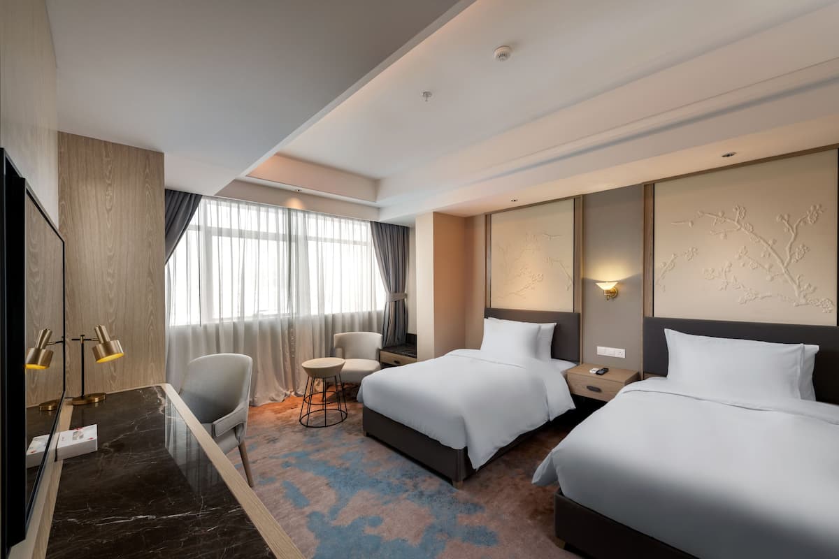 Ein Hotelzimmer mit zwei Betten, einem Schreibtisch mit Stuhl, einem kleinen runden Tisch und einem Fernseher.
