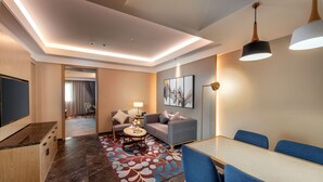 Habitación de hotel moderna con zona de comedor, sofá, mesa de centro y televisor.