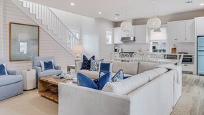 Un salon moderne avec un escalier, des meubles blancs et un coin cuisine.