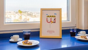 A framed welcome sign with a cartoon character, two cups of tea, and a slice of cake on a table by a window. - Appartamento all Arenella by Wonderful Italy (Naples)