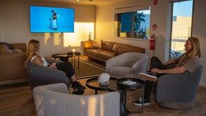 A modern living room with a large flat-screen TV, comfortable seating, and a small coffee table. - Mackay Adventure Lodge (Andergrove)