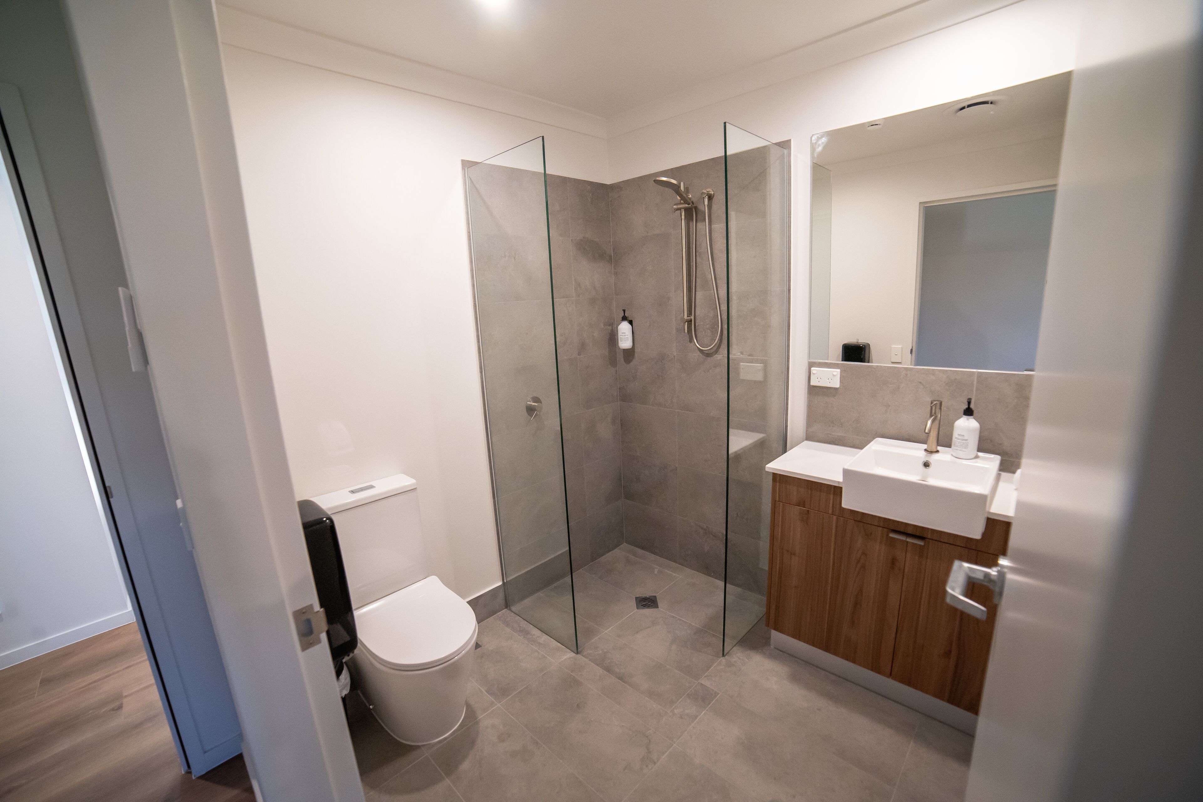 A modern bathroom with a glass-enclosed shower, a toilet, and a vanity with a sink and mirror.