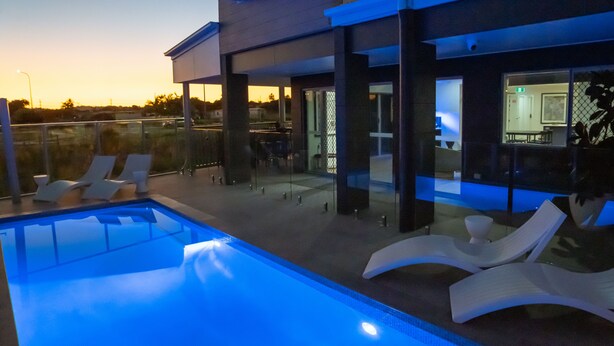 A modern outdoor pool area with lounge chairs and a glass-enclosed patio. - Mackay Adventure Lodge (Andergrove)