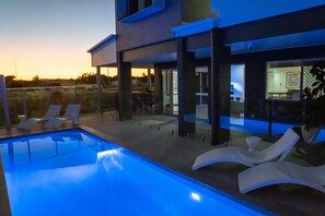 A modern outdoor pool area with lounge chairs and a glass-enclosed patio. - Mackay Adventure Lodge (Andergrove)