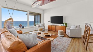 Ein modernes Wohnzimmer mit einer Ledersofa, einem Couchtisch und einem Fernseher. Ein großes Fenster bietet Blick auf den Ozean.