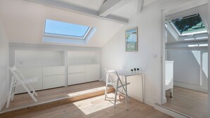 Une pièce lumineuse et blanche, dotée de fenêtres de toit, avec une petite table et des chaises, et offrant une vue sur l’extérieur.