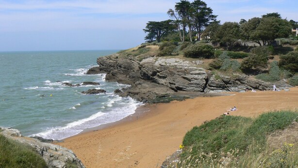 Une plage côtière bordée de falaises rocheuses et d’un rivage sablonneux.