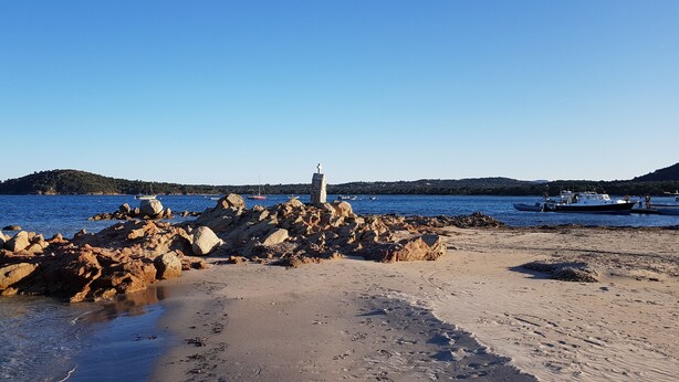 Una costa rocosa con un faro y barcos al fondo.