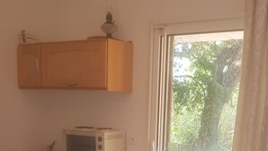 Una cocina con microondas, un refrigerador pequeño y un armario de madera. Hay una puerta corrediza de vidrio que da a un espacio exterior con una mesa y sillas.