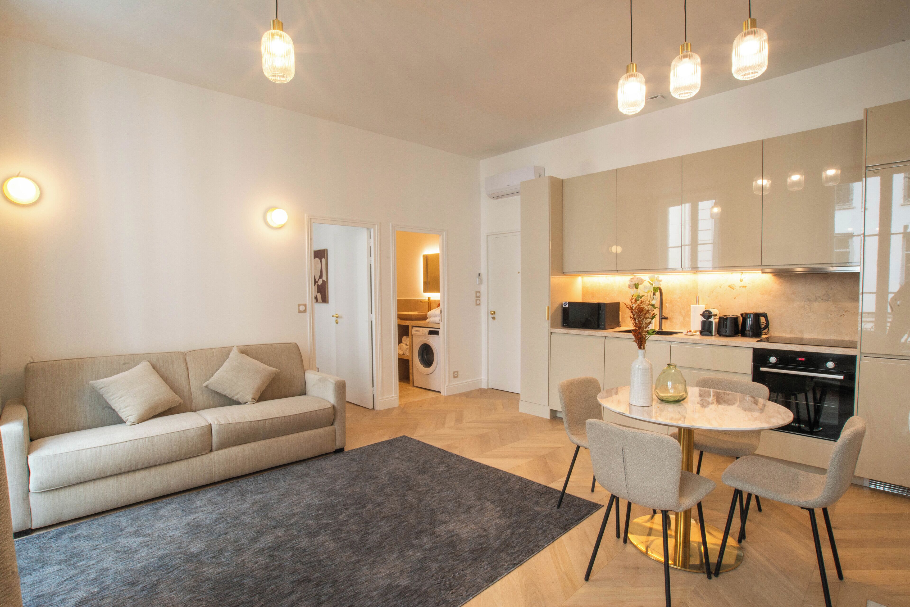 A modern kitchen with built-in appliances, a dining area with a round table and chairs, and a living area with a sofa and a rug.