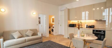 A modern kitchen with built-in appliances, a dining area with a round table and chairs, and a living area with a sofa and a rug.