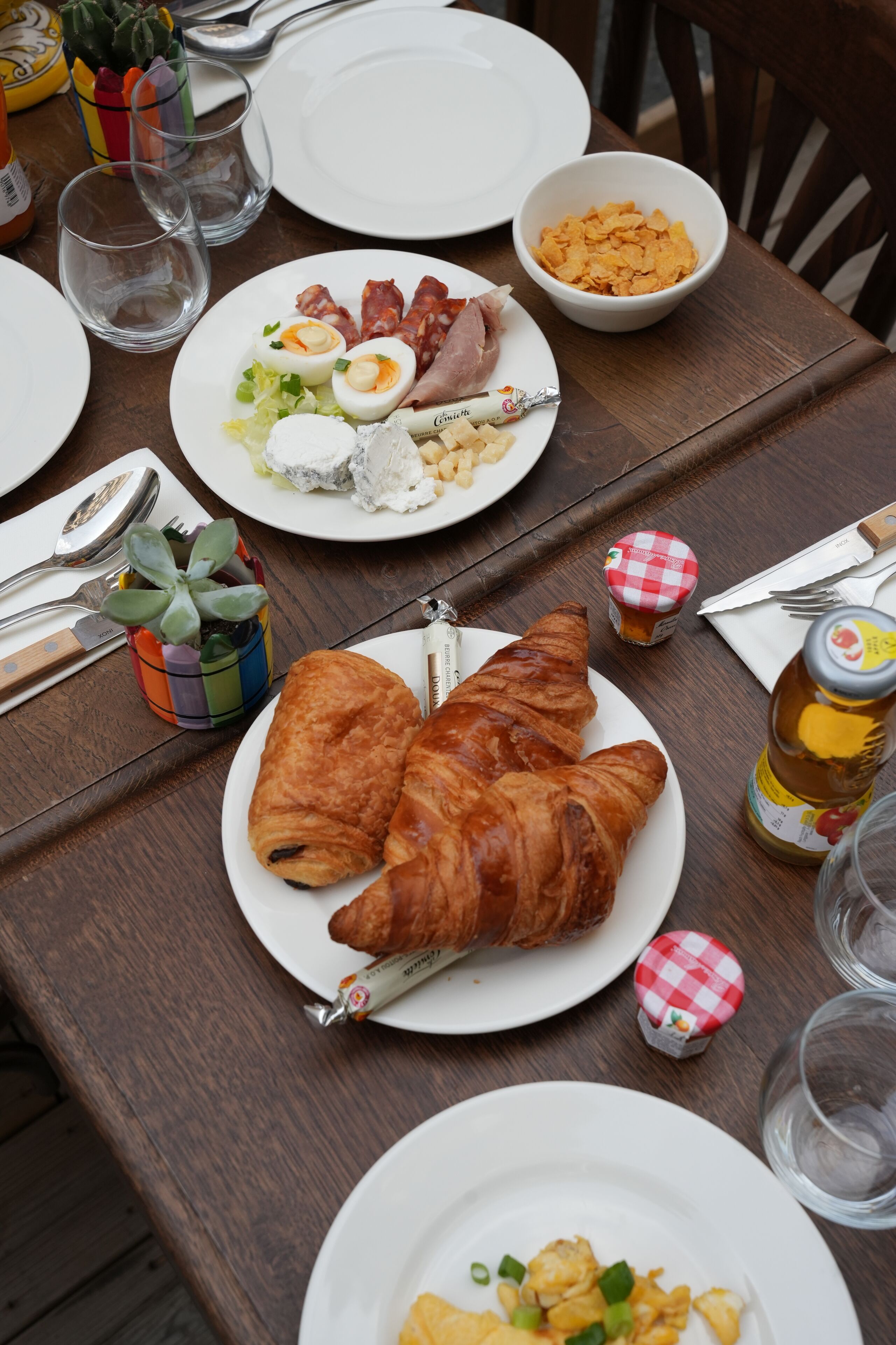 Una mesa servida con platos de comida, incluyendo cruasanes y huevos, y diferentes condimentos.
