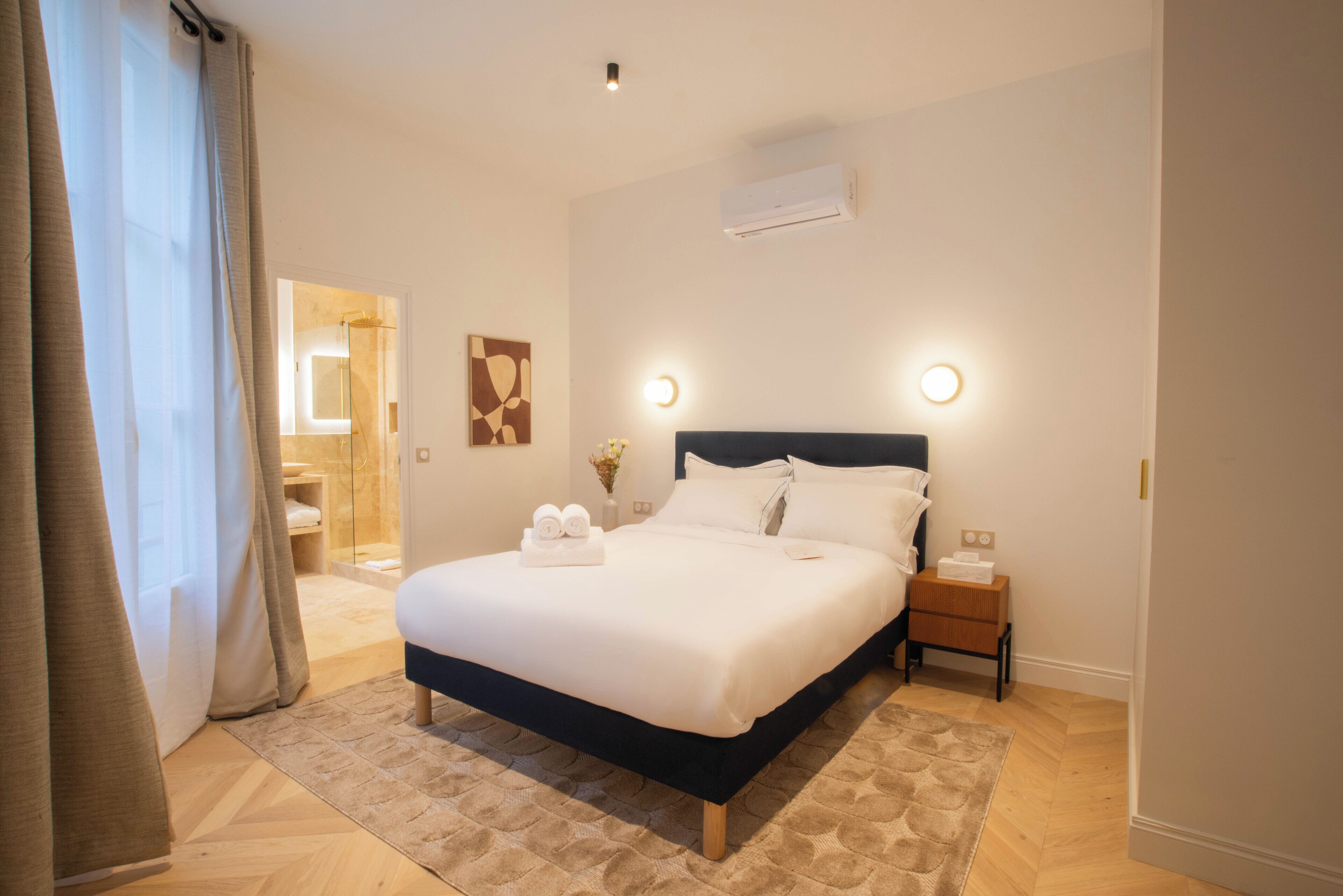 Una habitación de hotel con una cama grande, mesitas de noche y un baño visible a través de una puerta abierta.