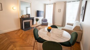 A modern living room with a round marble table, green upholstered chairs, a beige sofa, a fireplace, and a large window with curtains. - Aparthotel Quartier Libre Madeleine (Paris)