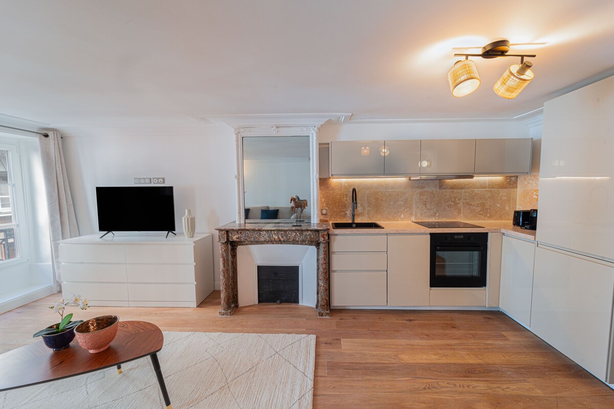 A modern kitchen with white cabinetry, a wooden dining table, a built-in TV, and a stone backsplash.
