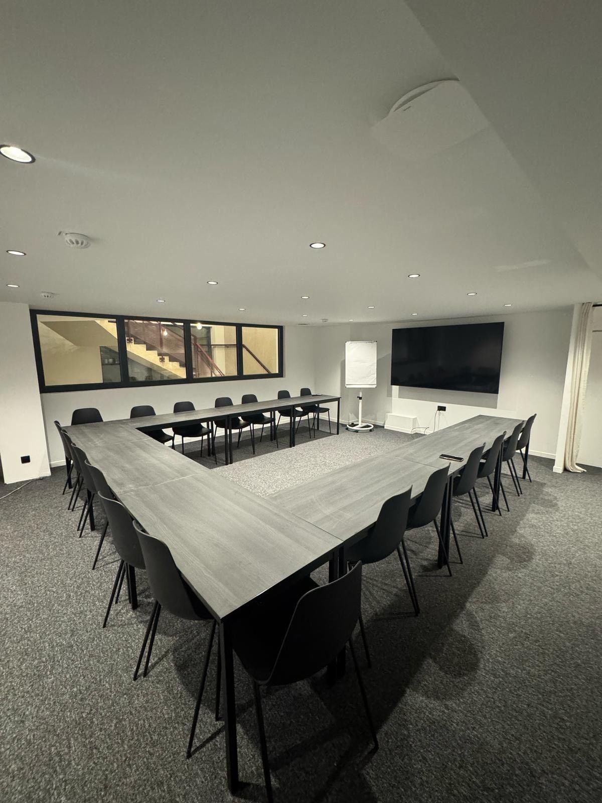 A conference room with a long table, chairs, a projector screen, and a large window.