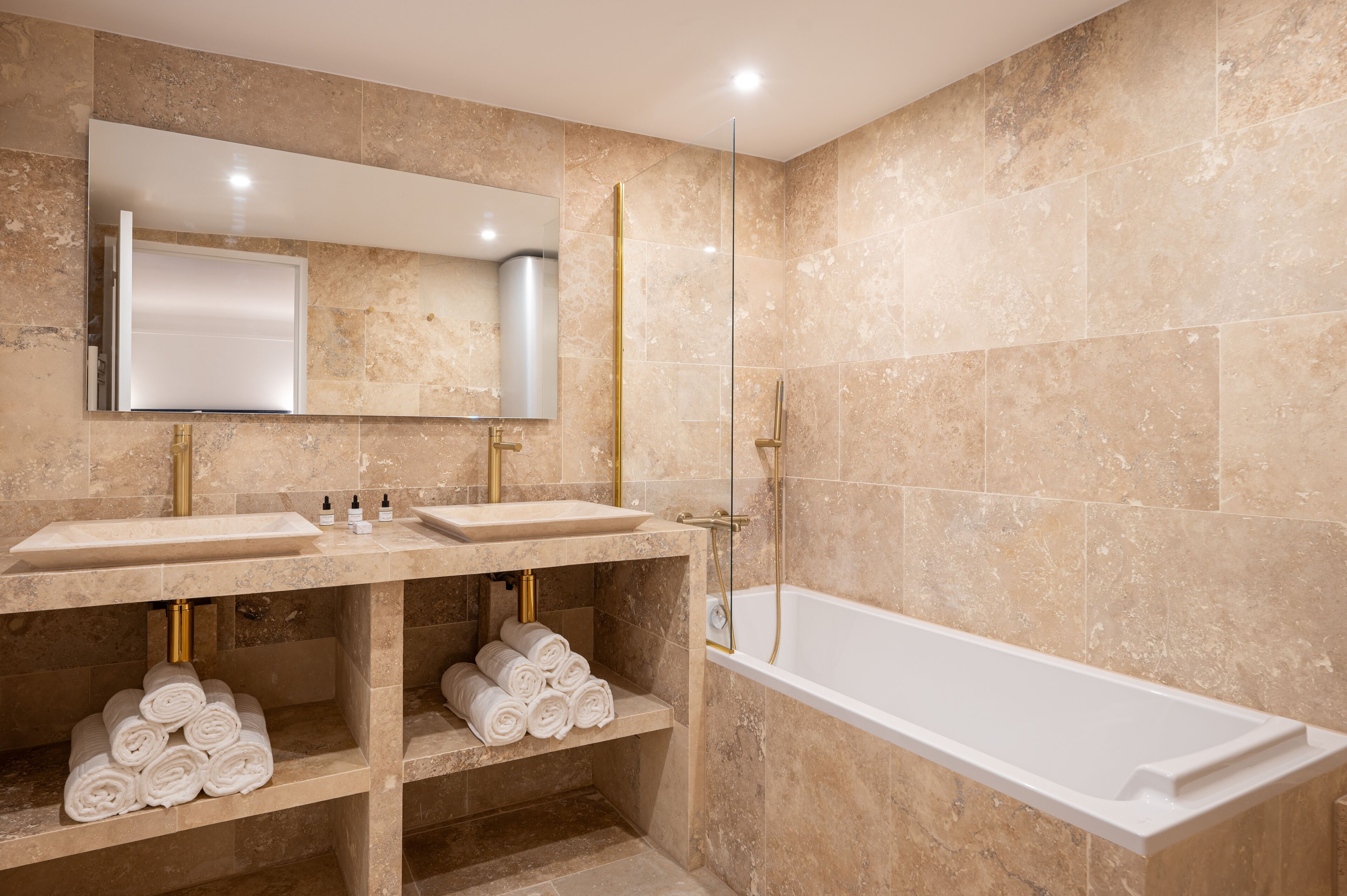 A modern bathroom with two sinks, a large mirror, a glass-enclosed shower, and shelves with neatly rolled towels.