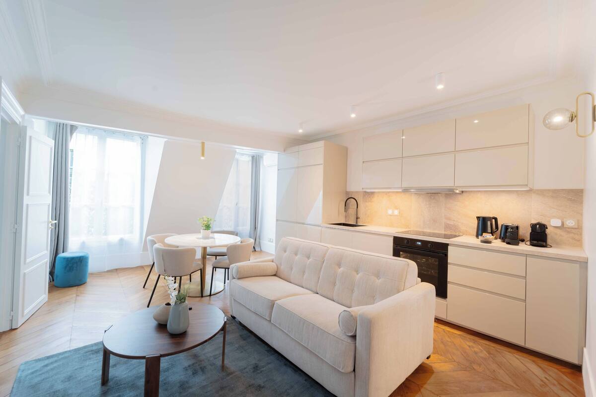 A modern kitchen with white cabinets, a dining area with a round table and chairs, and a living area with a sofa and a coffee table.