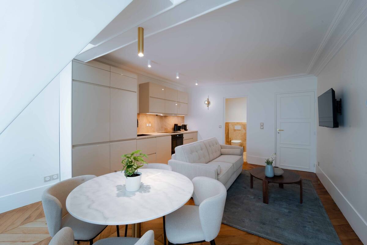 A modern living room with a marble table, grey sofas, and a kitchen in the background.