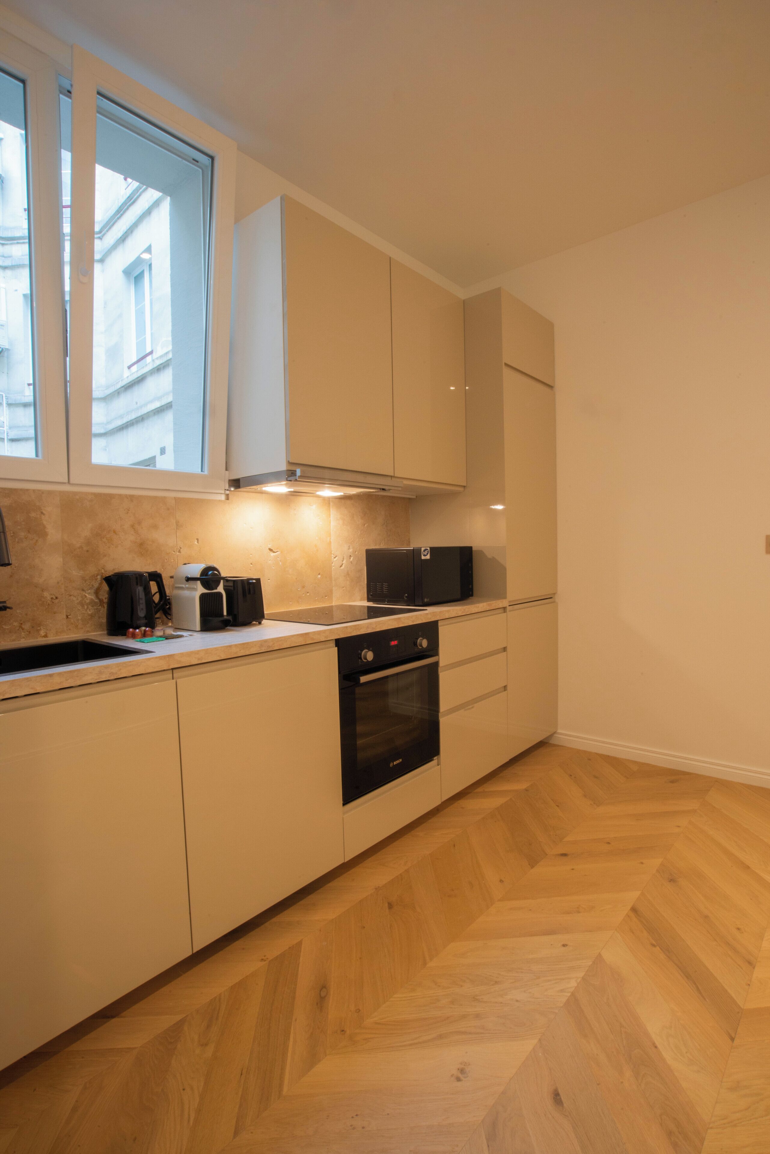A compact kitchen with a herringbone wooden floor, white cabinets, a built-in oven, and a microwave.