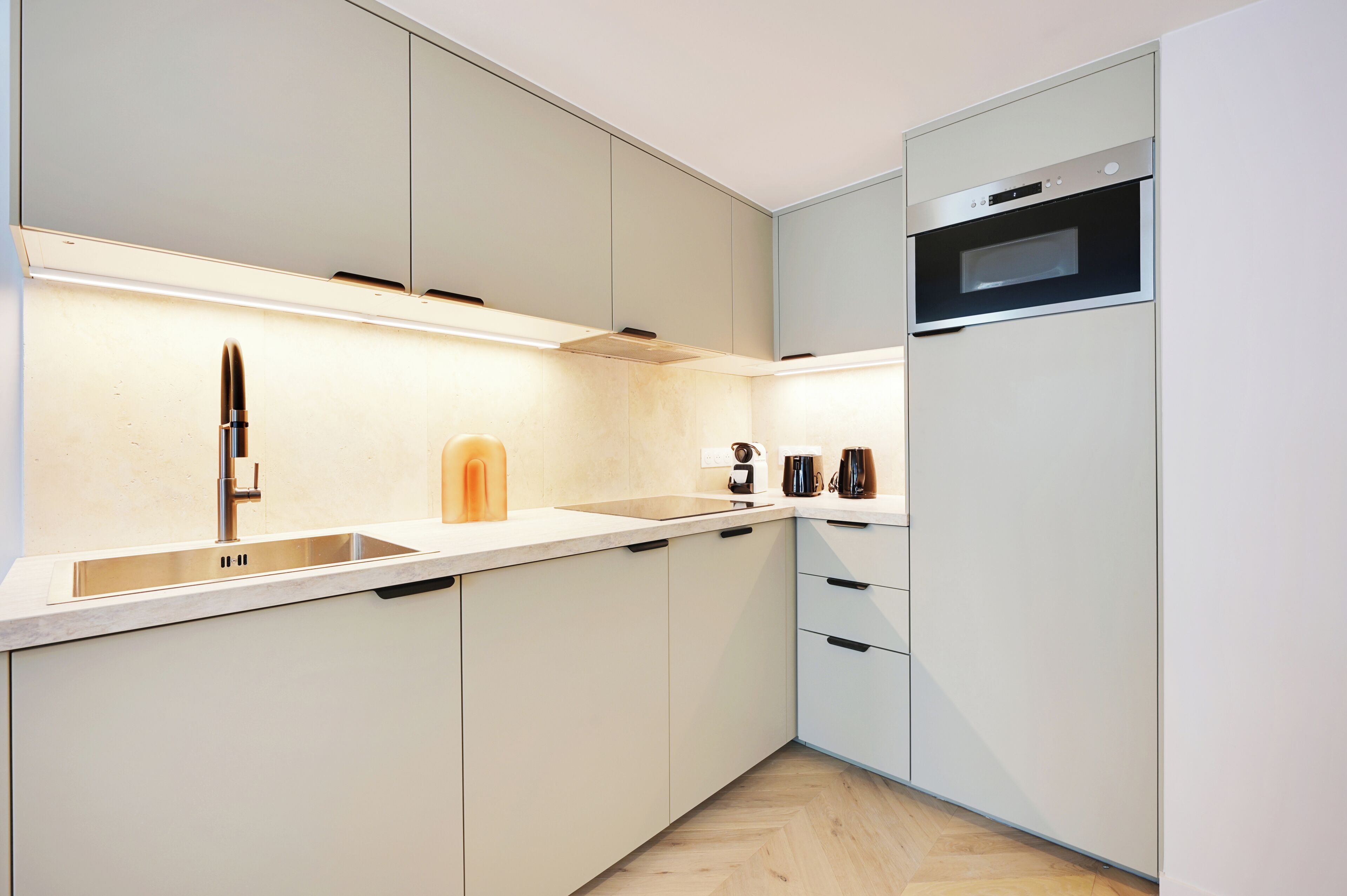 A modern kitchen with white cabinets, a stainless steel sink, a built-in oven, and a coffee maker.