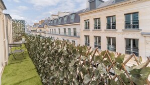 A row of townhouses with a green hedge and a small table with a chair in the foreground. - Aparthotel Quartier Libre Madeleine (Paris)