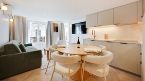 A modern kitchen with a round dining table and chairs, a sofa, and a TV mounted above the counter. - Aparthotel Quartier Libre Madeleine (Paris)