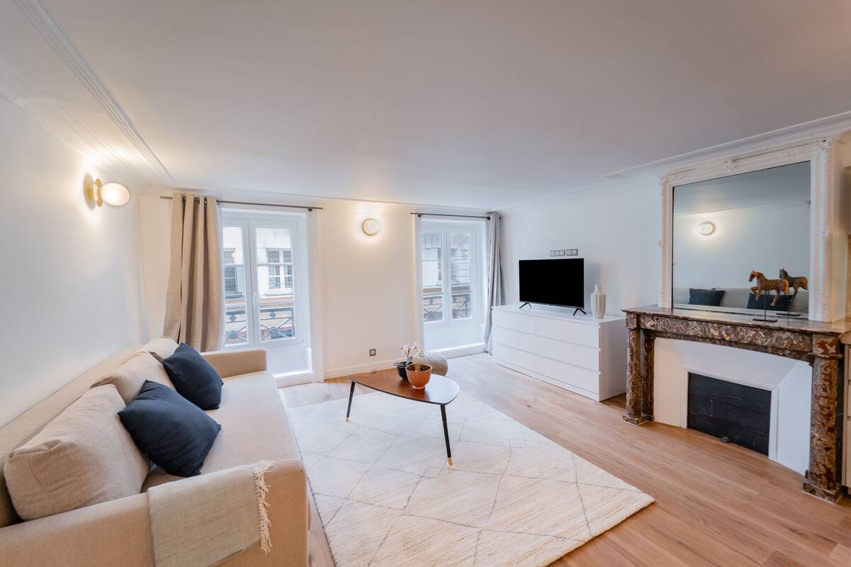 A modern living room with a sofa, coffee table, TV, fireplace, and large windows.