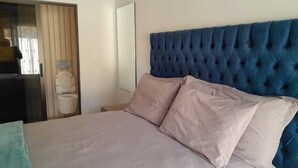 Una cama con cabecera capitonada, dos almohadas y una colcha de color claro.