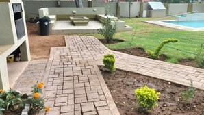 Un patio trasero con un camino de ladrillos, una piscina pequeña y un jardín con plantas y flores.
