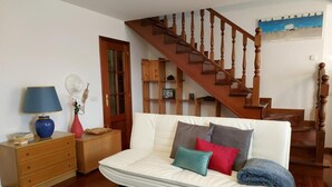 Un salón con un sofá blanco, mesitas de madera, una lámpara azul y una escalera de madera.