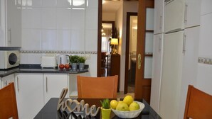 Una cocina con gabinetes blancos, una mesa de comedor con sillas, un tazón de limones y una pequeña planta en maceta.