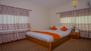 Een netjes ingerichte slaapkamer met een houten bed, twee kussens, een nachtkastje met een lamp en kamergordijnen met een patroon.